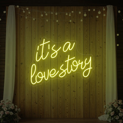 Photo of the 'It’s a Love Story' neon sign glowing in lemon yellow against a styled interior wall.