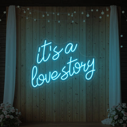 Photo of the 'It’s a Love Story' neon sign glowing in ice blue against a styled interior wall.