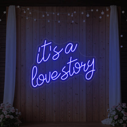 Photo of the 'It’s a Love Story' neon sign glowing in deep blue against a styled interior wall.