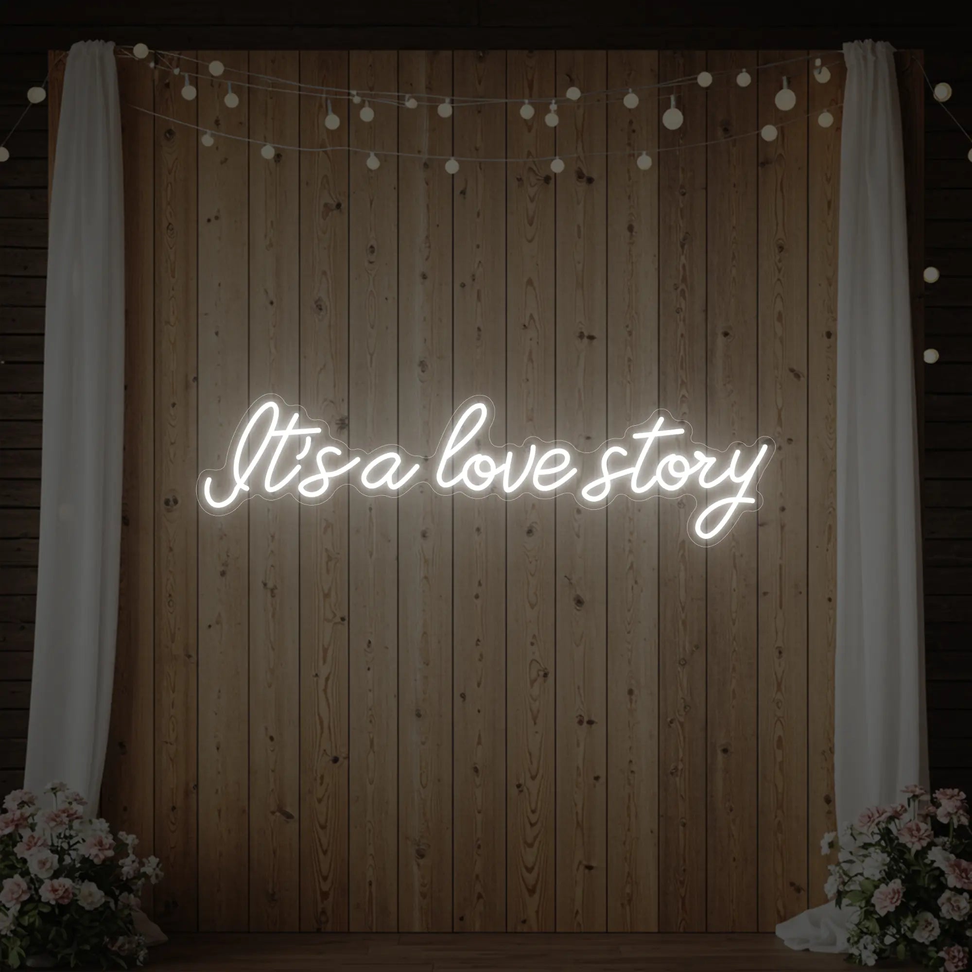 Photo of the 'It’s A Love Story' neon sign glowing in cool white against a styled interior wall.