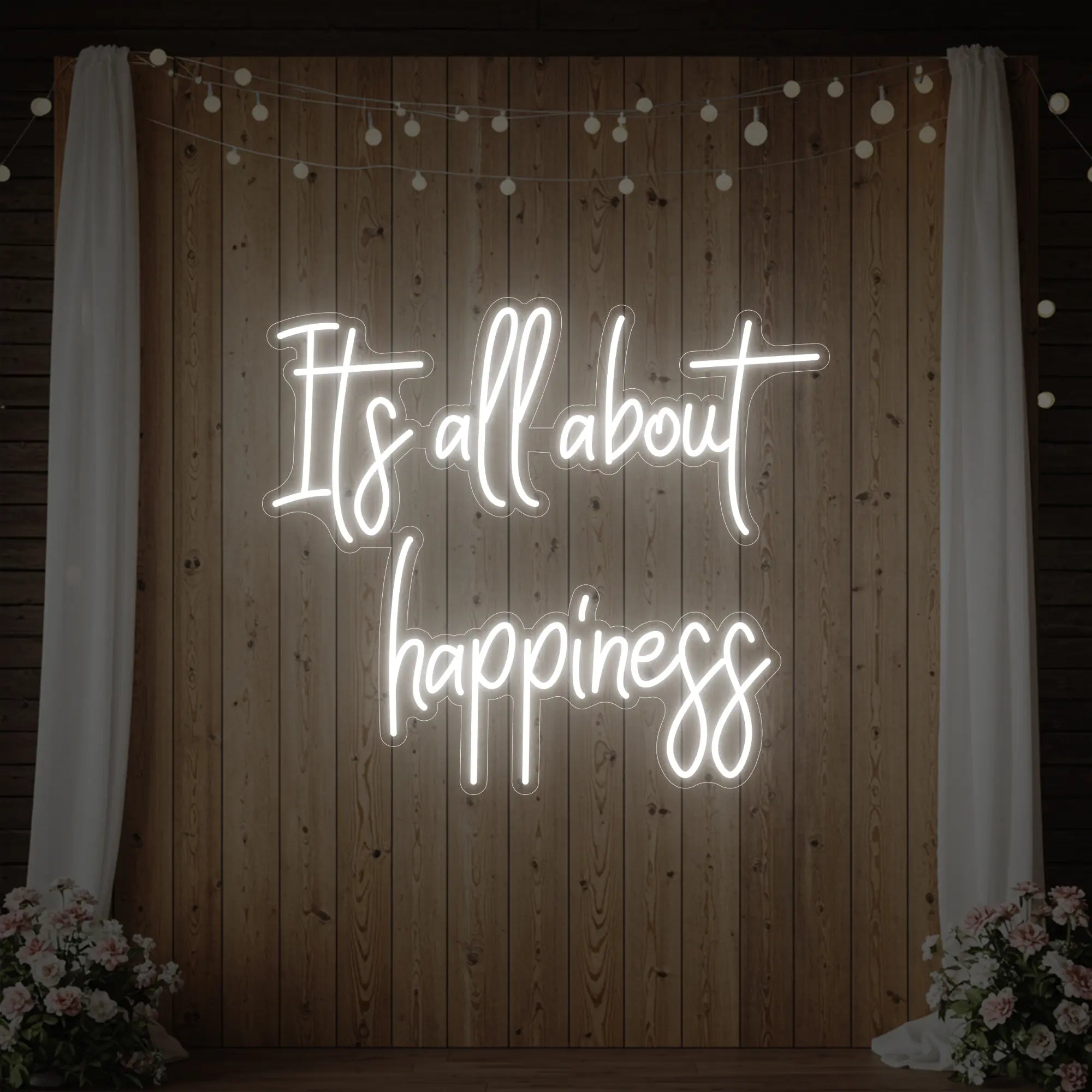 Photo of the 'It’s All About Happiness' neon sign glowing in cool white against a styled interior wall.