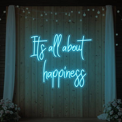 Photo of the 'It’s All About Happiness' neon sign glowing in ice blue against a styled interior wall.