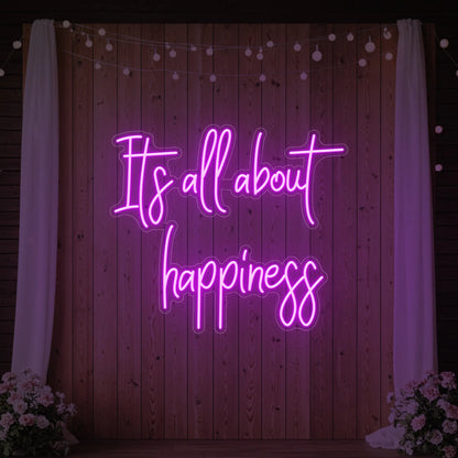 Photo of the 'It’s All About Happiness' neon sign glowing in deep pink against a styled interior wall.