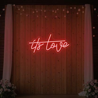 Photo of the 'It’s Love' neon sign glowing in red against a styled interior wall.