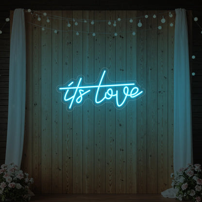 Photo of the 'It’s Love' neon sign glowing in ice blue against a styled interior wall.