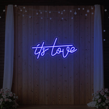 Photo of the 'It’s Love' neon sign glowing in deep blue against a styled interior wall.