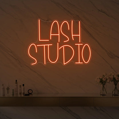 Photo of the 'LASH STUDIO' neon sign glowing in golden yellow against a styled interior wall.