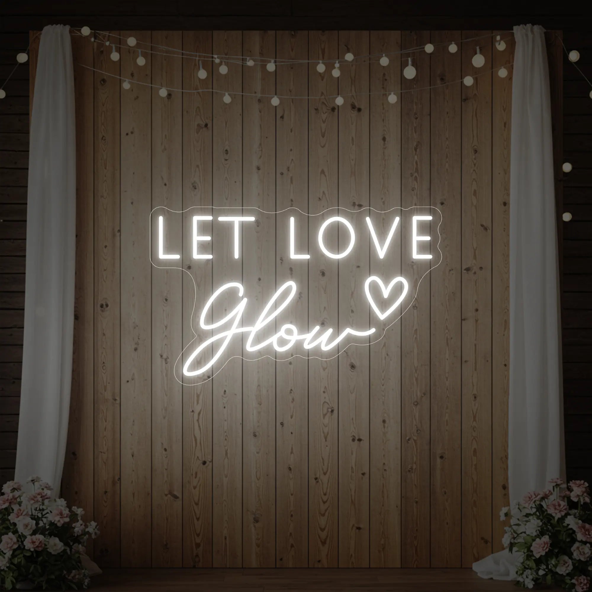 Photo of the 'Let Love Glow' neon sign glowing in cool white against a styled interior wall.