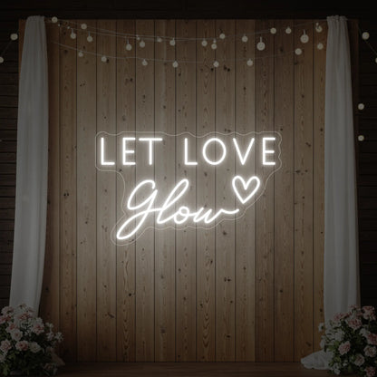 Photo of the 'Let Love Glow' neon sign glowing in cool white against a styled interior wall.