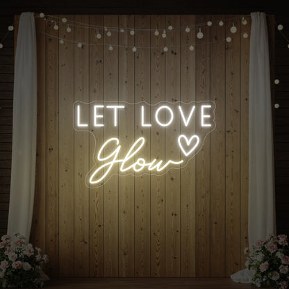Photo of the 'Let Love Glow' neon sign glowing in warm white against a styled interior wall.