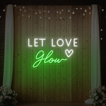 Photo of the 'Let Love Glow' neon sign glowing in green against a styled interior wall.