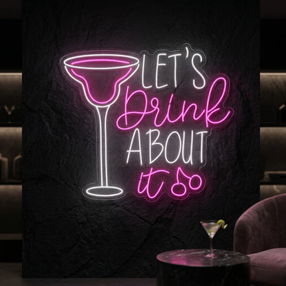 Photo of the 'Let's Drink About It' neon sign glowing in multi-color against a styled interior wall.