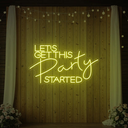Photo of the 'Let’s Get This Party Started' neon sign glowing in lemon yellow against a styled interior wall.
