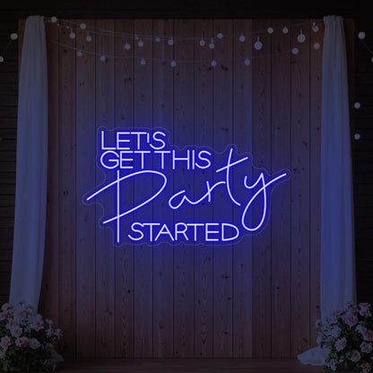 Photo of the 'Let’s Get This Party Started' neon sign glowing in deep blue against a styled interior wall.