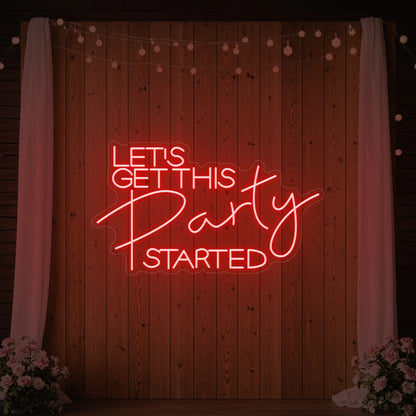 Photo of the 'Let’s Get This Party Started' neon sign glowing in red against a styled interior wall.