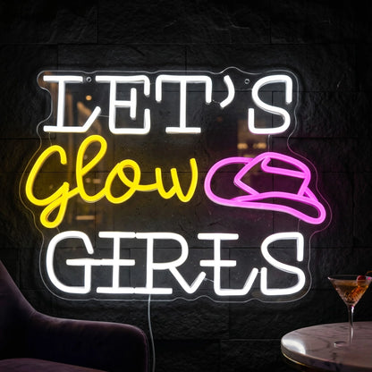 Photo of the 'Let's Glow Girls' neon sign glowing in multi-color against a styled interior wall.