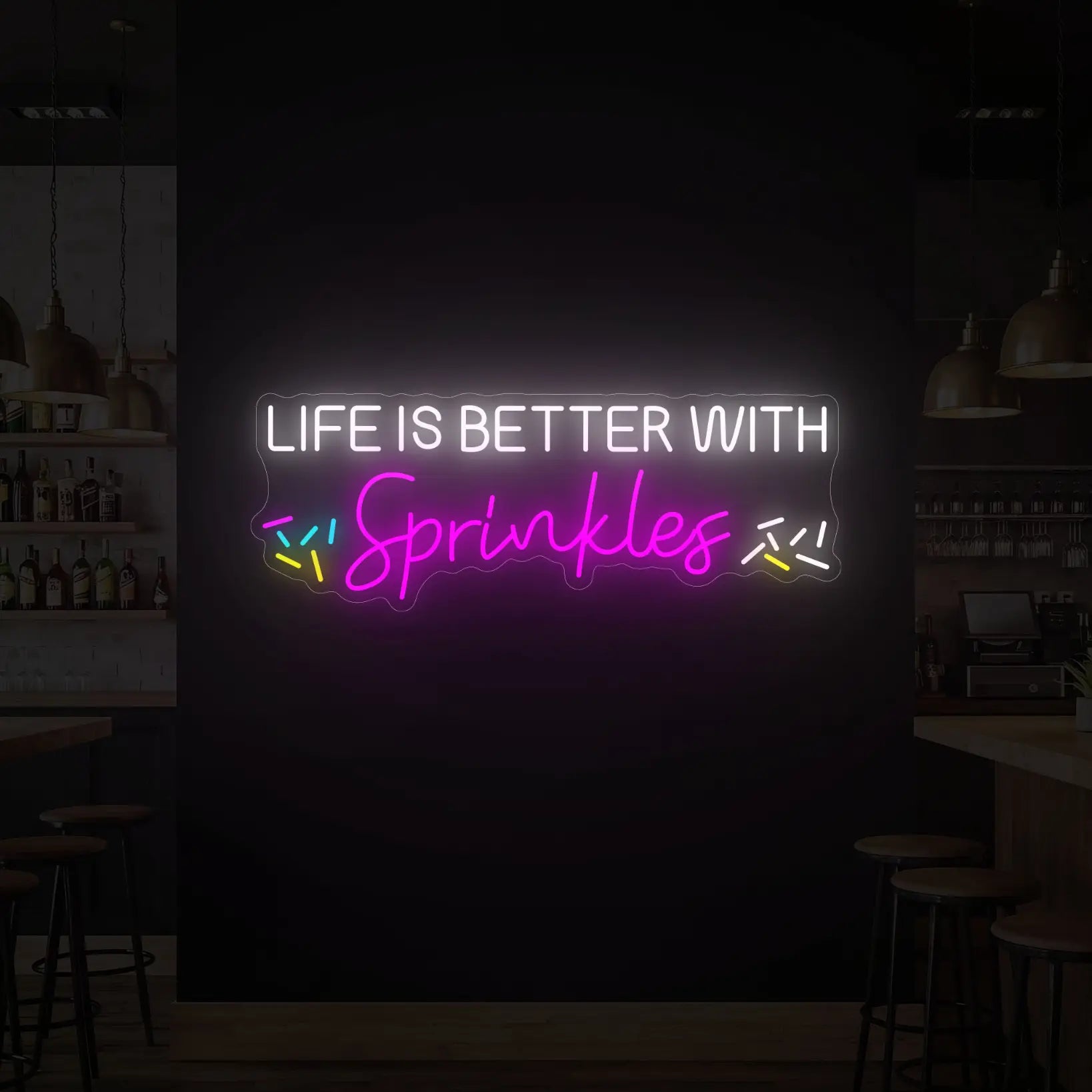 Photo of the 'LIFE IS BETTER WITH SPRINKLES' neon sign glowing in multi-color against a styled interior wall.