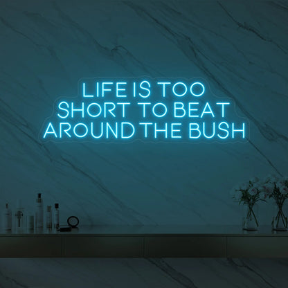 Photo of the 'Life is too short to beat around the bush' neon sign glowing in ice blue against a marble wall.