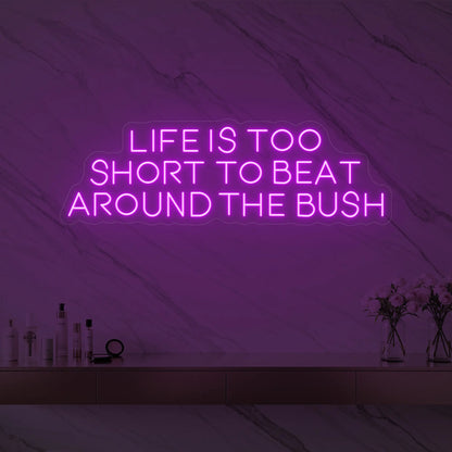 Photo of the 'Life is too short to beat around the bush' neon sign glowing in deep pink against a marble wall.