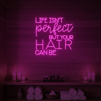 Photo of the 'Life isn’t perfect but your hair can be' neon sign glowing in light pink against a wood-paneled spa wall.