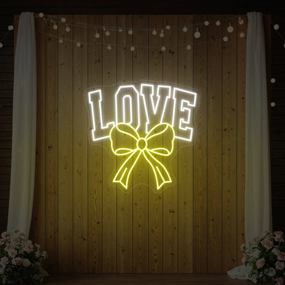 Photo of the 'Love and Ribbon' neon sign glowing in lemon yellow against a styled interior wall.