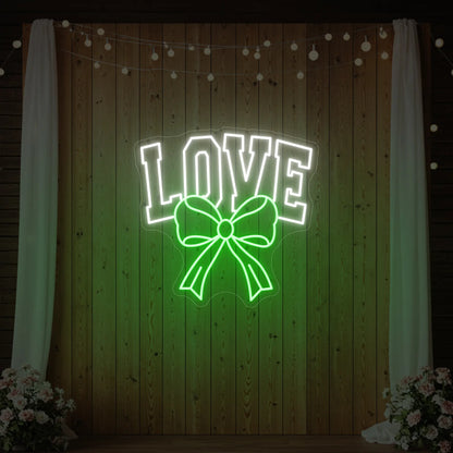 Photo of the 'Love and Ribbon' neon sign glowing in green against a styled interior wall.