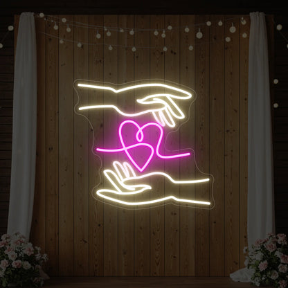 Photo of the 'Love Hands' neon sign glowing in light pink and cool white against a styled interior wall.