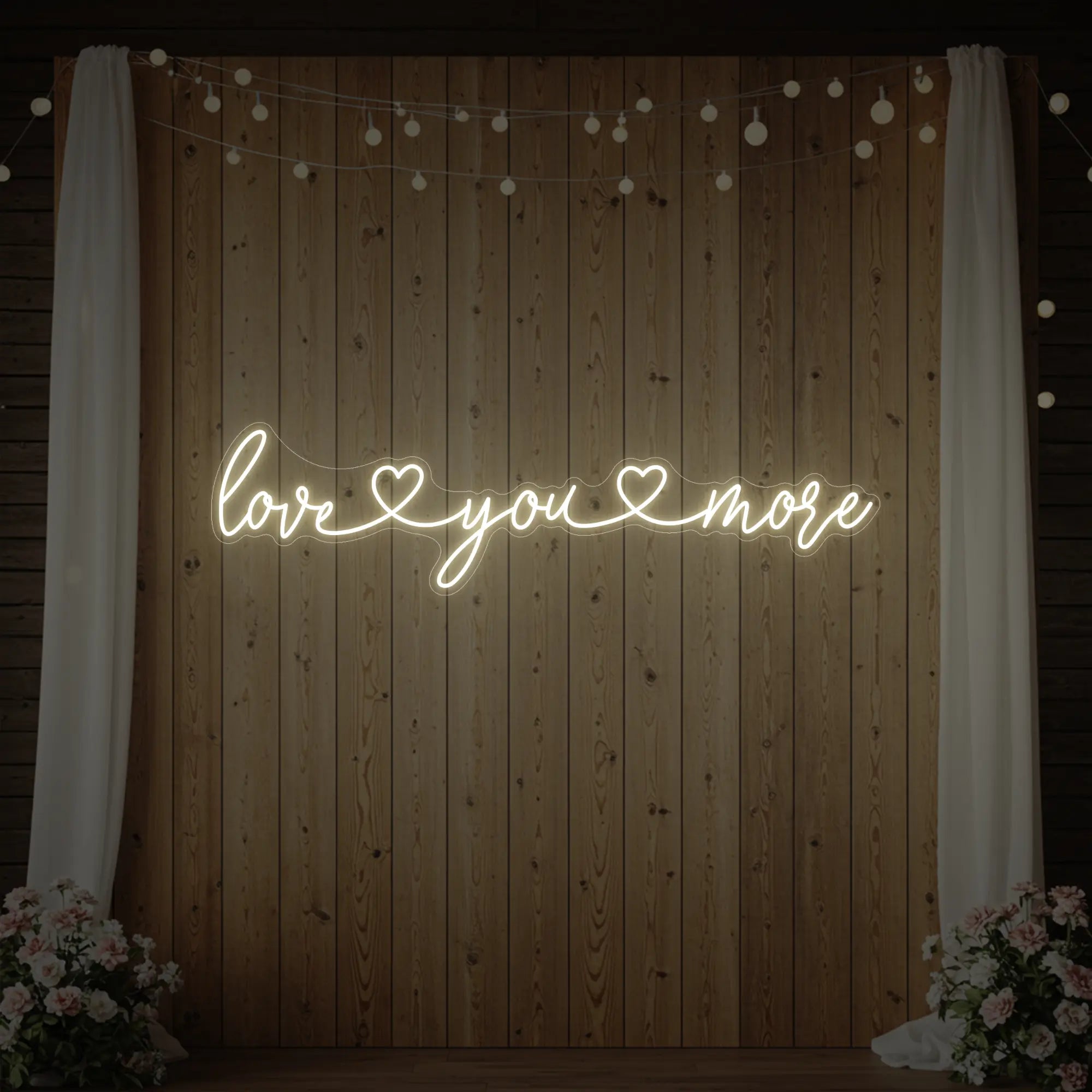 Photo of the 'Love You More' neon sign glowing in warm white against a styled interior wall.