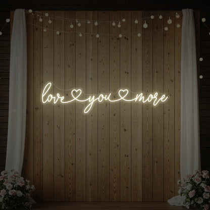 Photo of the 'Love You More' neon sign glowing in warm white against a styled interior wall.