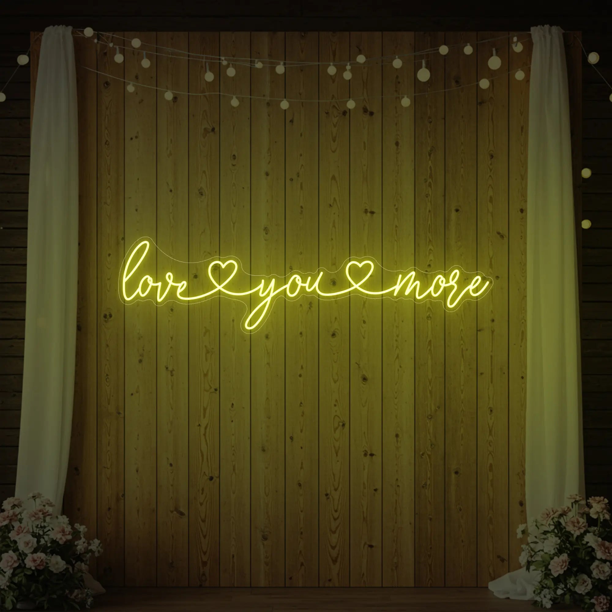 Photo of the 'Love You More' neon sign glowing in lemon yellow against a styled interior wall.