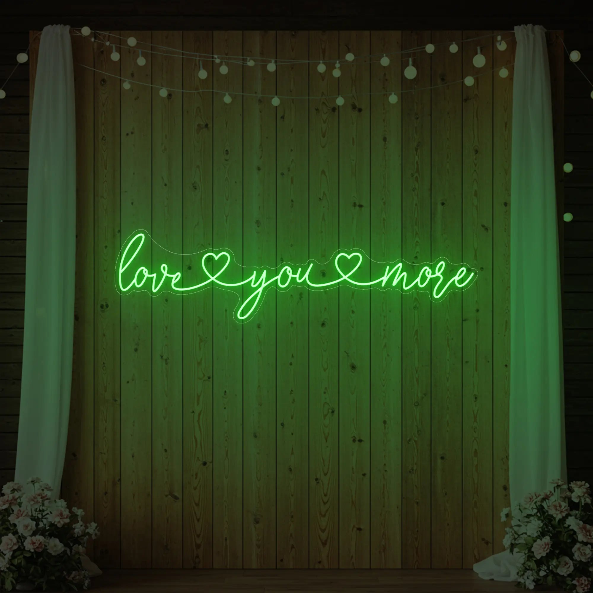 Photo of the 'Love You More' neon sign glowing in green against a styled interior wall.