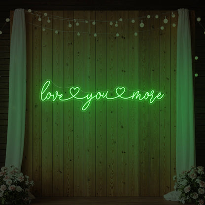 Photo of the 'Love You More' neon sign glowing in green against a styled interior wall.
