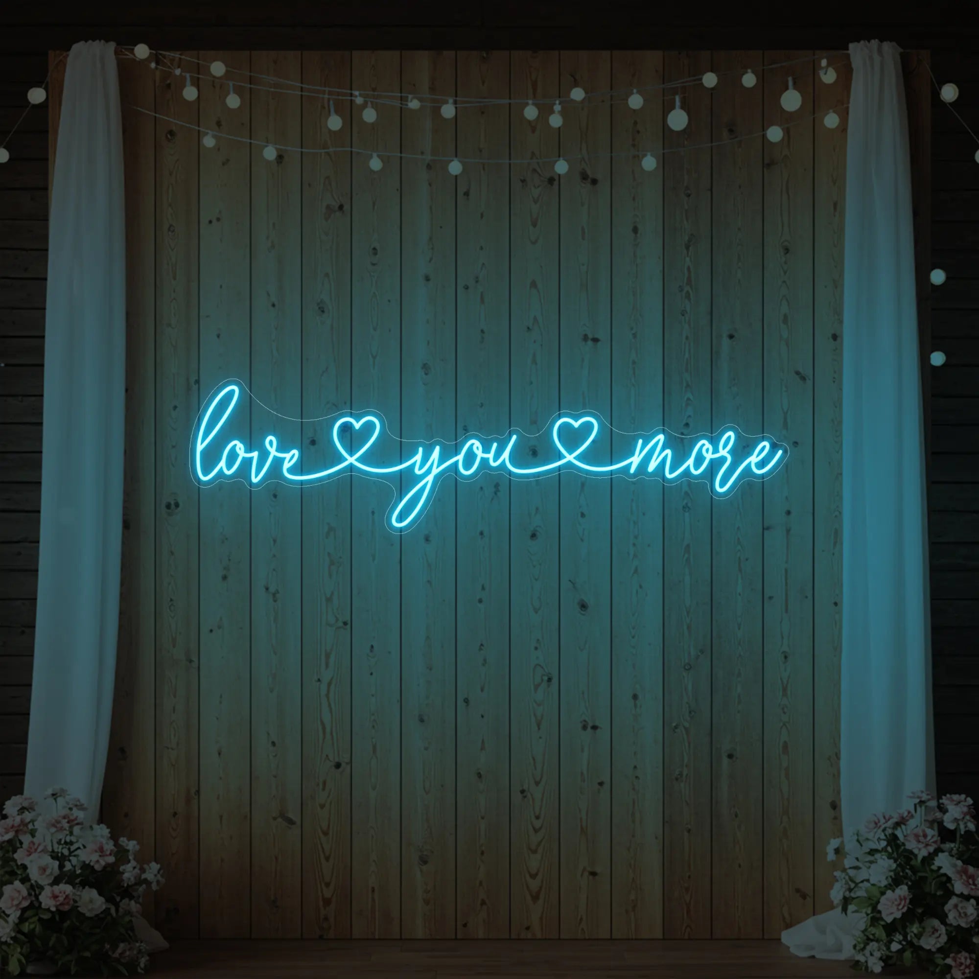 Photo of the 'Love You More' neon sign glowing in ice blue against a styled interior wall.