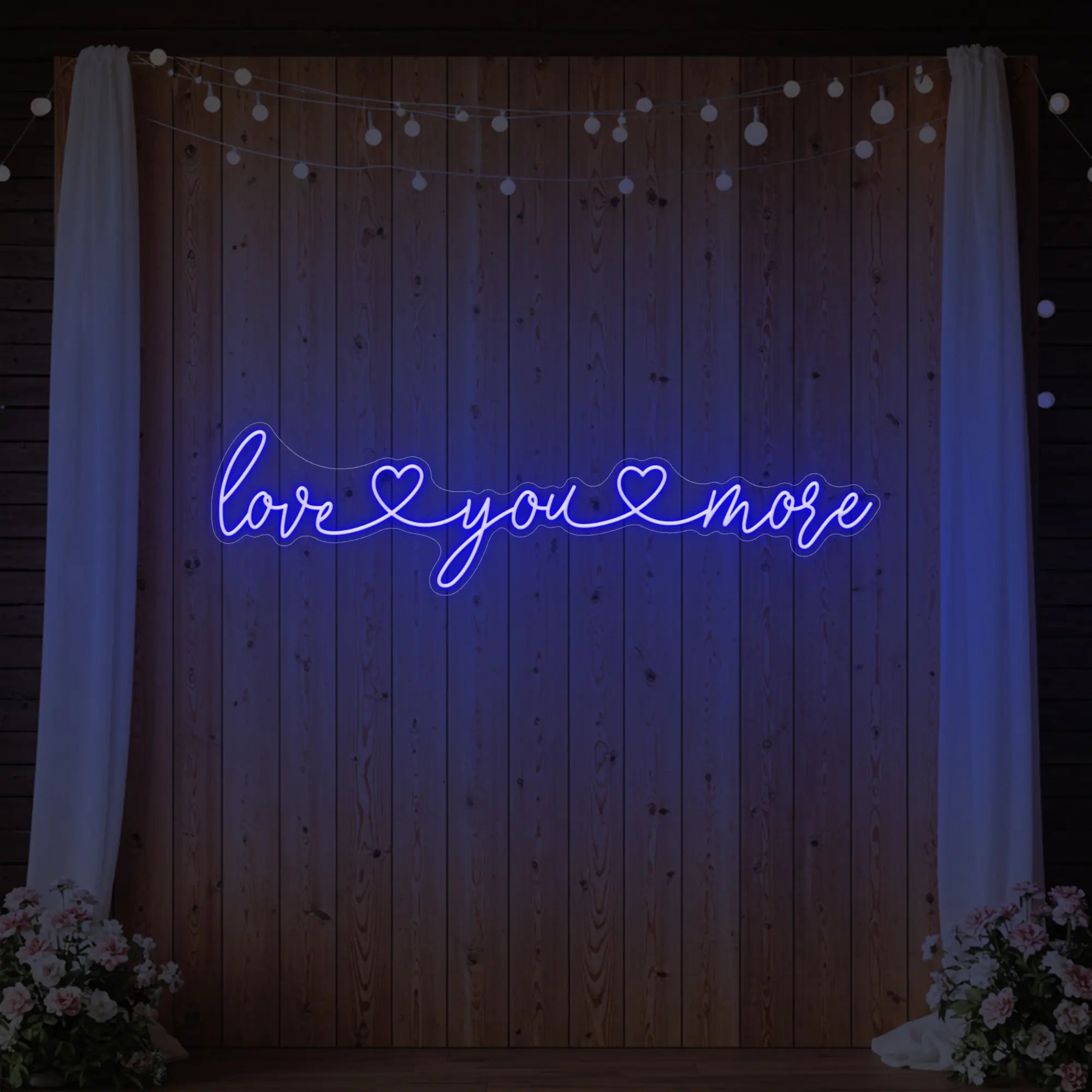 Photo of the 'Love You More' neon sign glowing in deep blue against a styled interior wall.