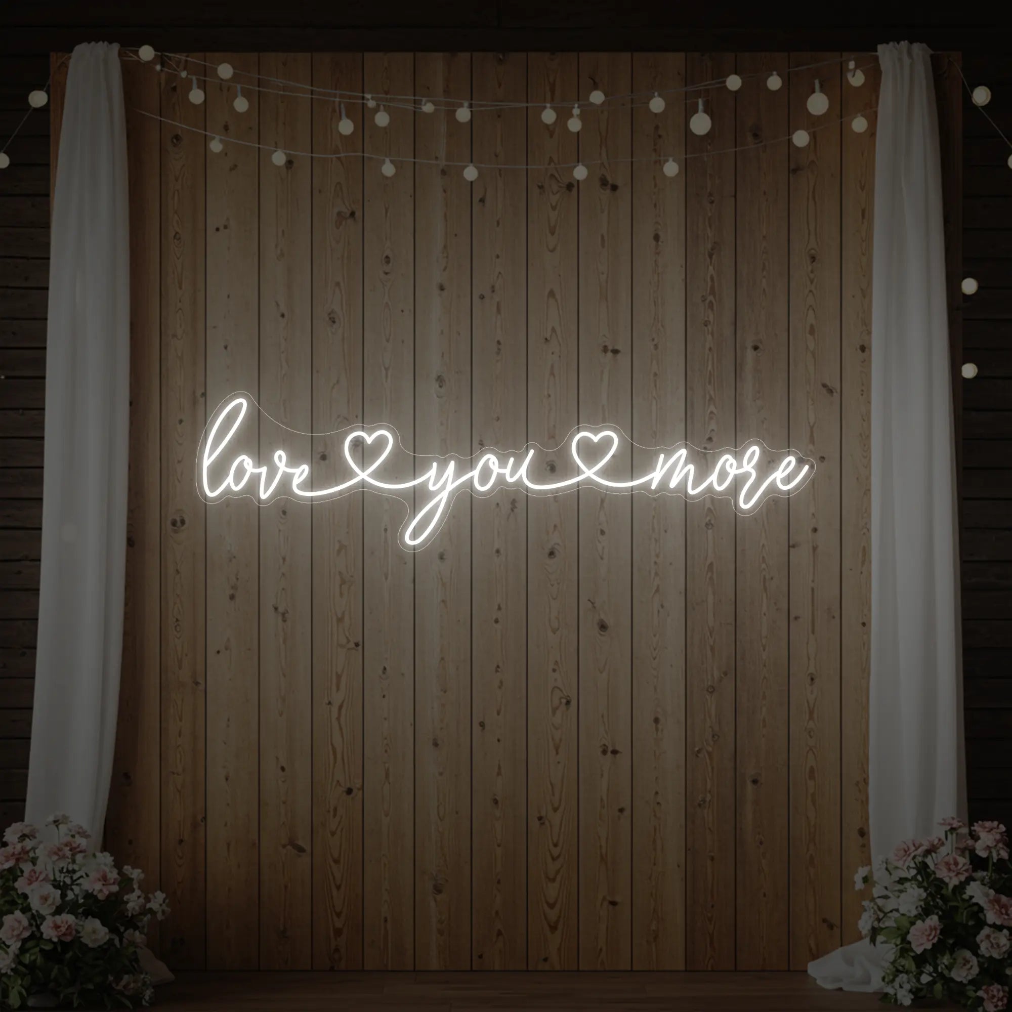 Photo of the 'Love You More' neon sign glowing in cool white against a styled interior wall.