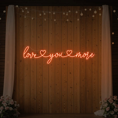 Photo of the 'Love You More' neon sign glowing in golden yellow against a styled interior wall.