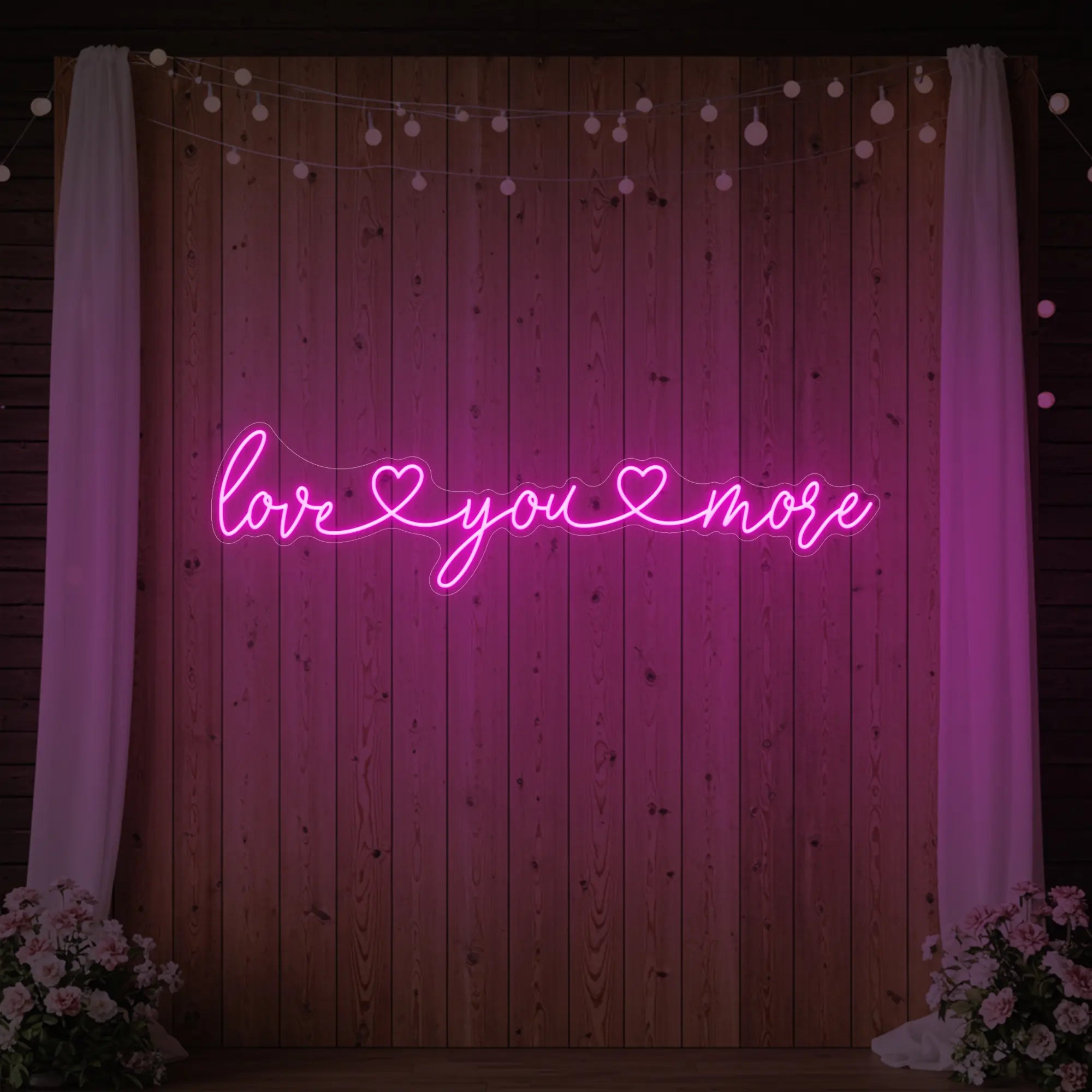 Photo of the 'Love You More' neon sign glowing in light pink against a styled interior wall.