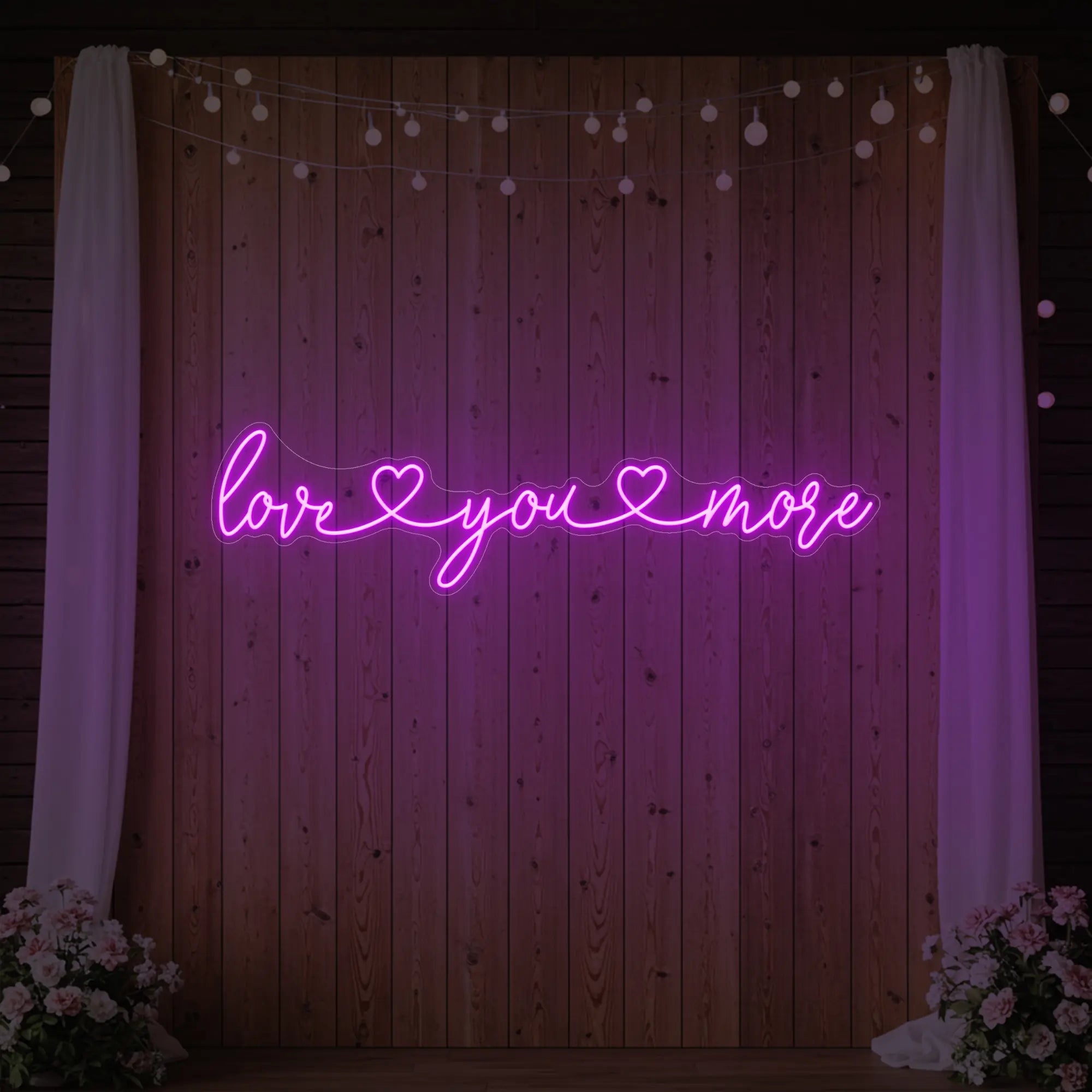 Photo of the 'Love You More' neon sign glowing in deep pink against a styled interior wall.