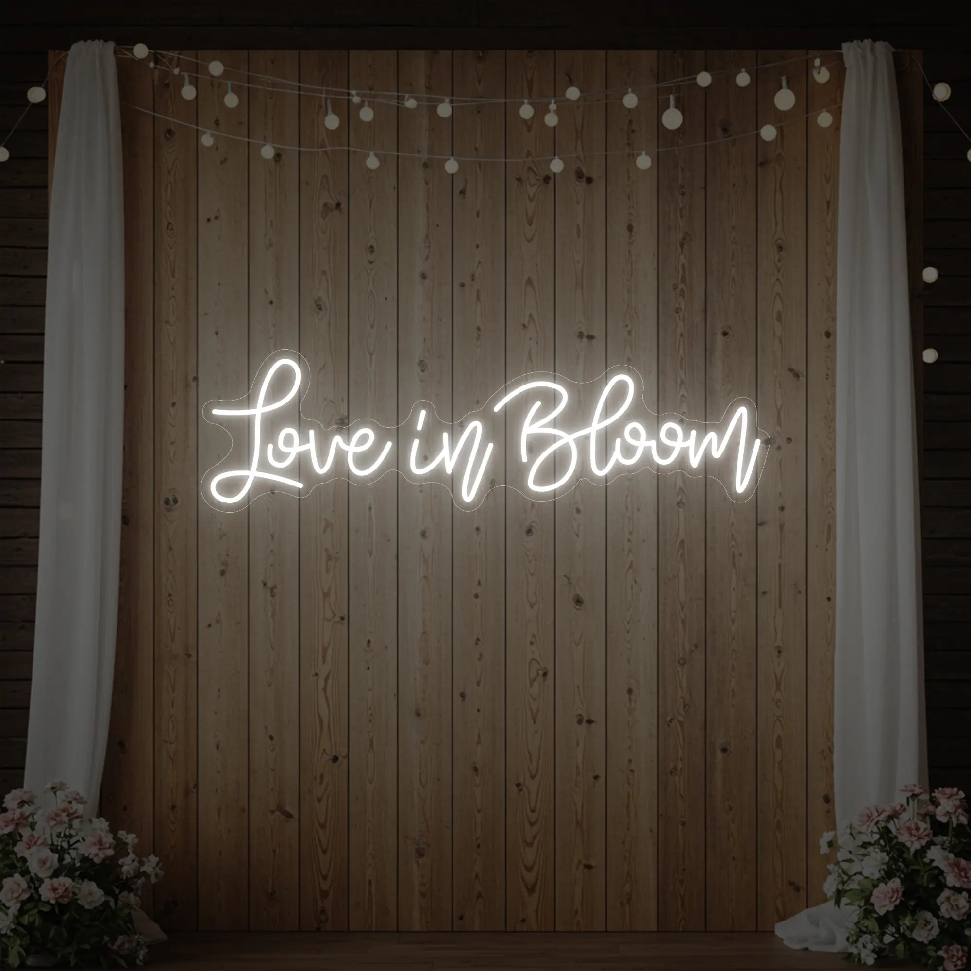 Photo of the 'Love in Bloom' neon sign glowing in cool white against a styled interior wall.