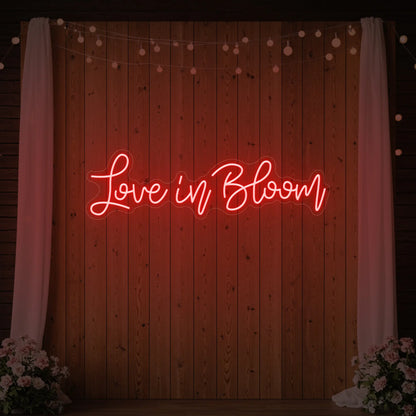 Photo of the 'Love in Bloom' neon sign glowing in red against a styled interior wall.