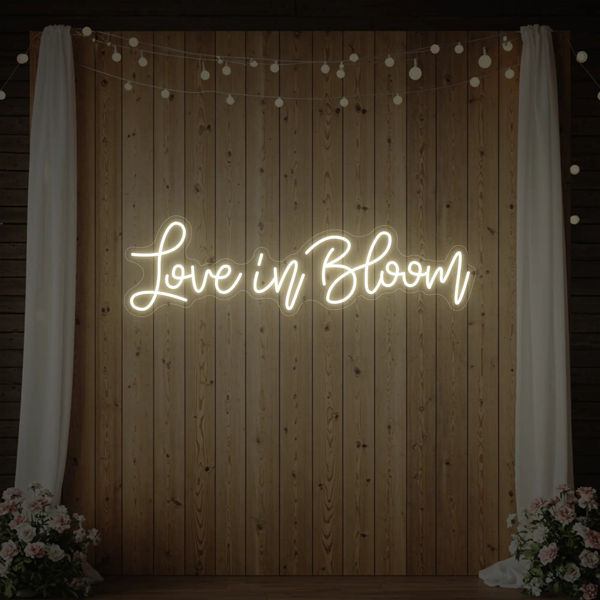 Photo of the 'Love in Bloom' neon sign glowing in warm white against a styled interior wall.