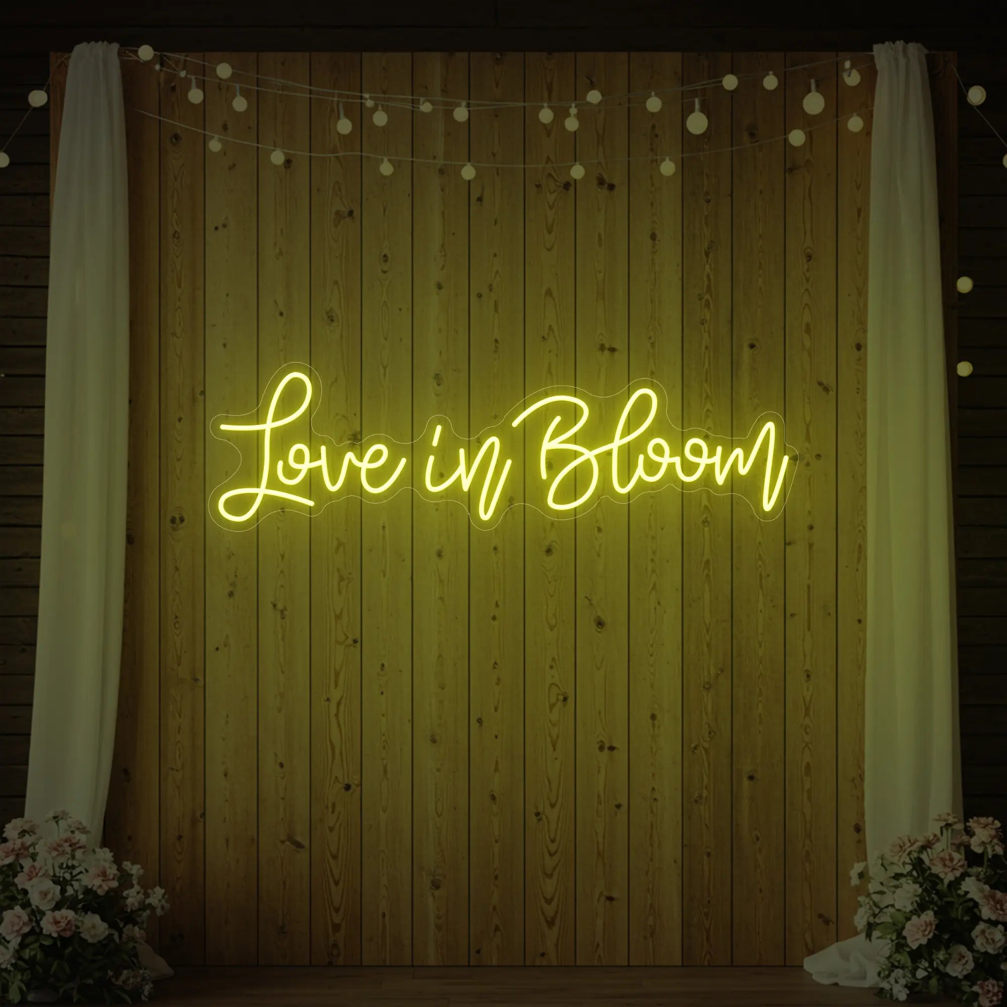 Photo of the 'Love in Bloom' neon sign glowing in lemon yellow against a styled interior wall.