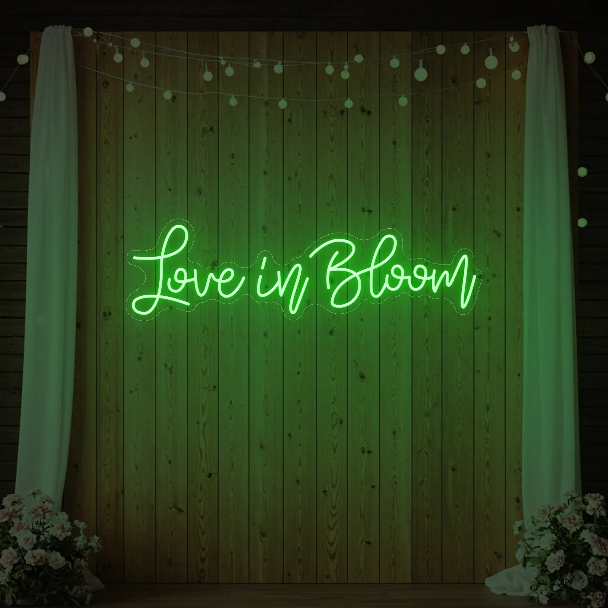 Photo of the 'Love in Bloom' neon sign glowing in green against a styled interior wall.