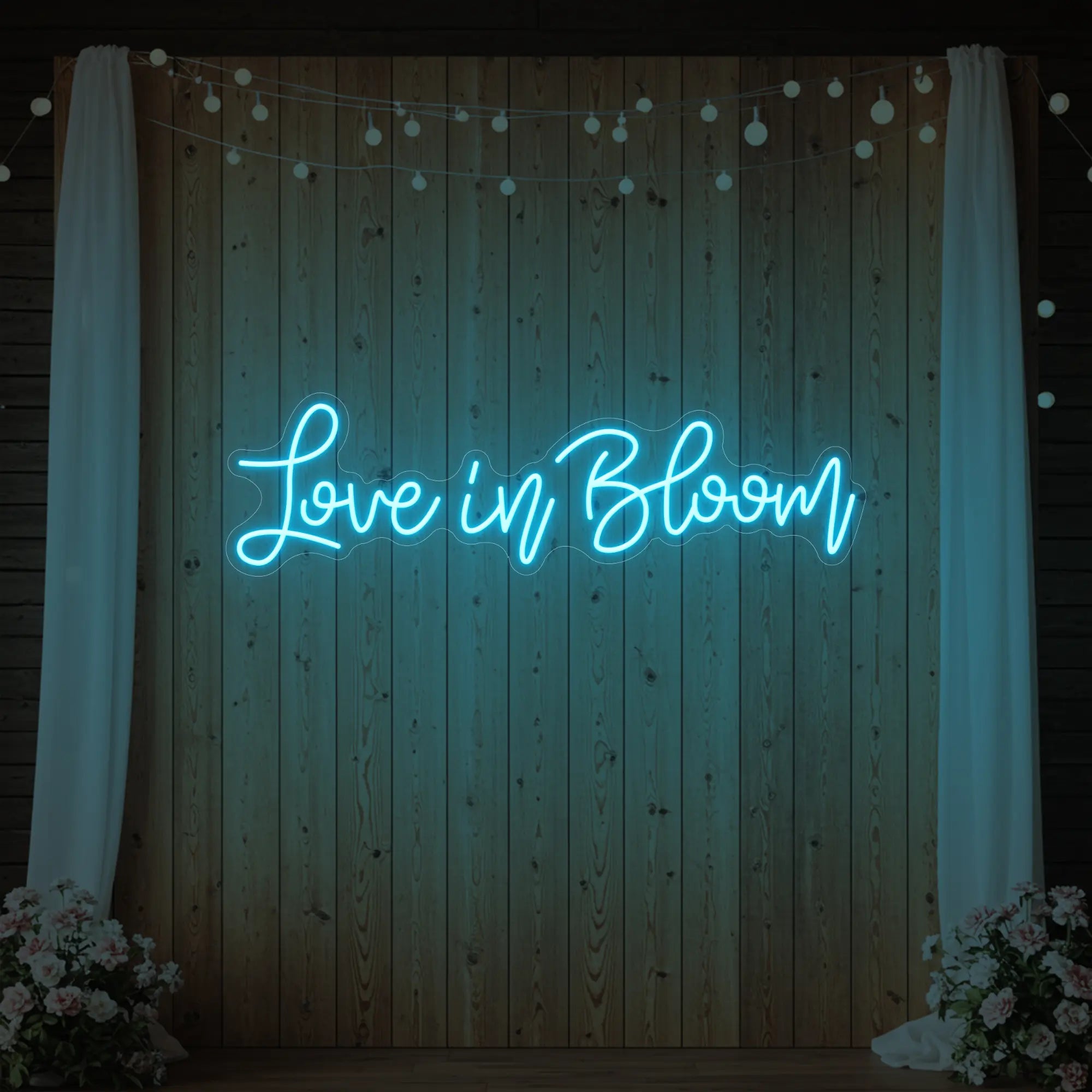 Photo of the 'Love in Bloom' neon sign glowing in ice blue against a styled interior wall.