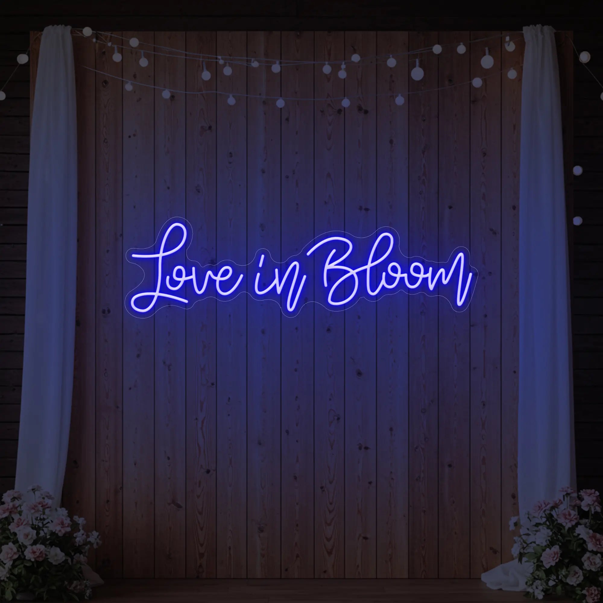 Photo of the 'Love in Bloom' neon sign glowing in deep blue against a styled interior wall.