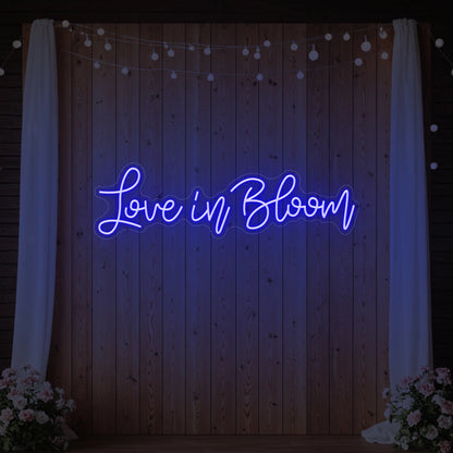 Photo of the 'Love in Bloom' neon sign glowing in deep blue against a styled interior wall.