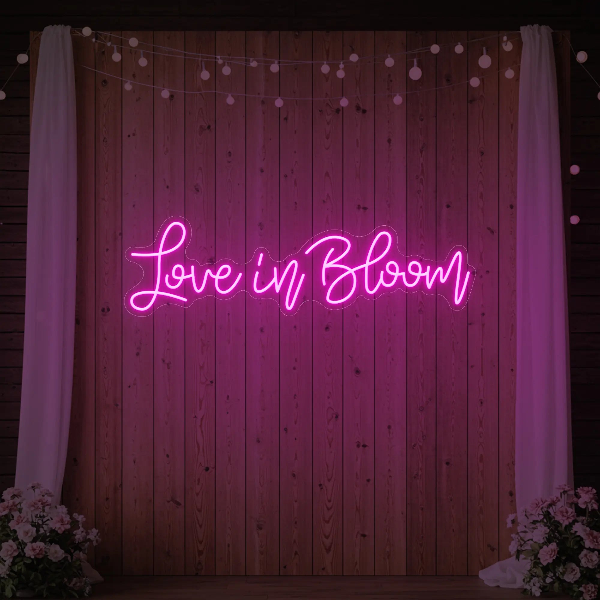 Photo of the 'Love in Bloom' neon sign glowing in light pink against a styled interior wall.