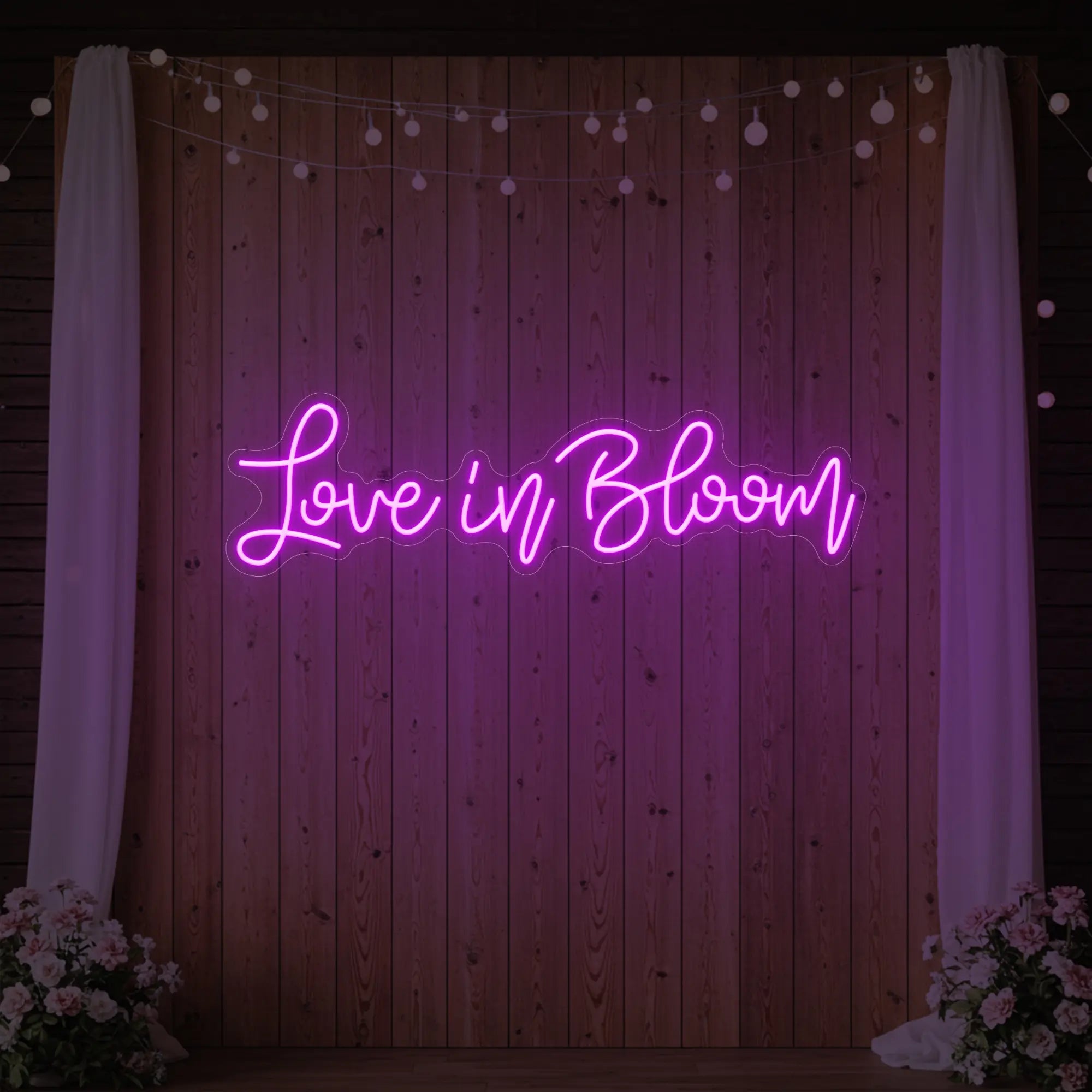 Photo of the 'Love in Bloom' neon sign glowing in deep pink against a styled interior wall.