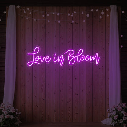 Photo of the 'Love in Bloom' neon sign glowing in deep pink against a styled interior wall.