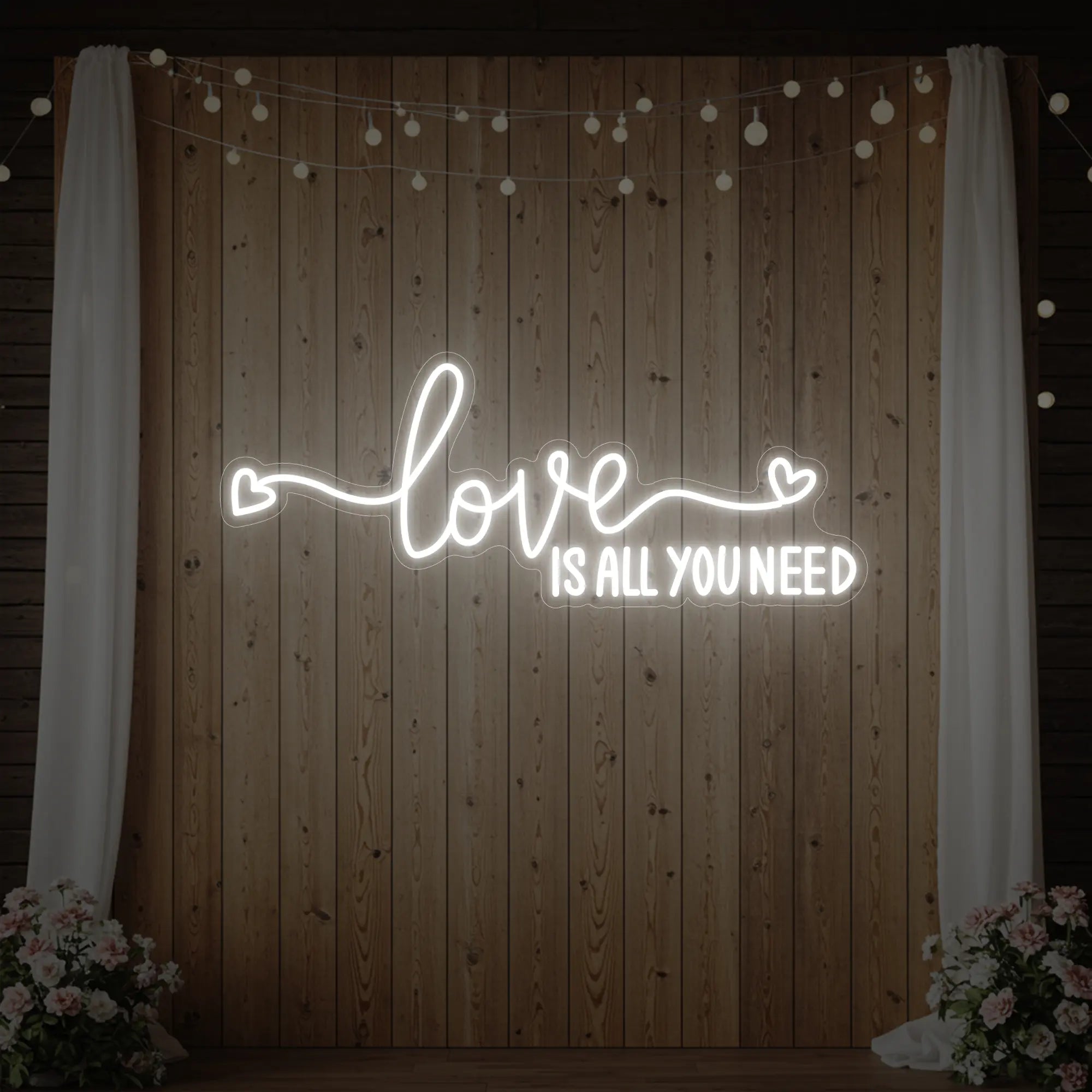 Photo of the 'Love Is All You Need' neon sign glowing in cool white against a styled interior wall.